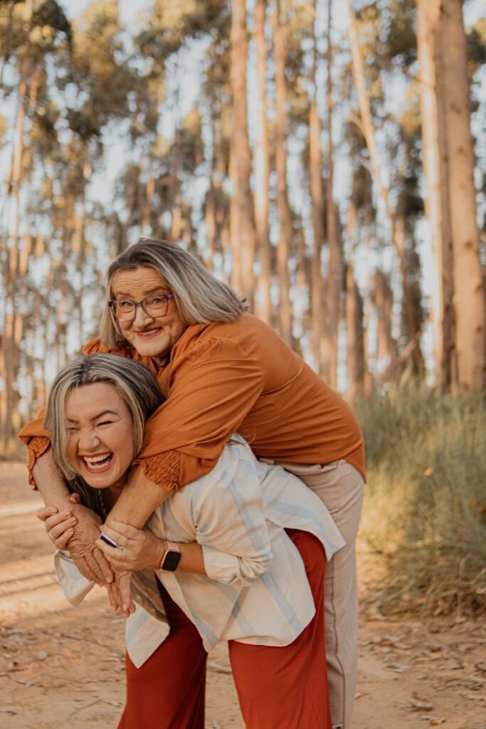 pexels-photo-24513644-24513644 Two women sharing a joyful piggyback ride in a lush, sunlit forest, expressing happiness and connection.